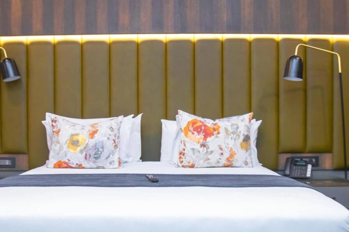 Habitación de hotel con cama, dos almohadas de estampado floral, mesita de noche con teléfono y lámpara de pared.
