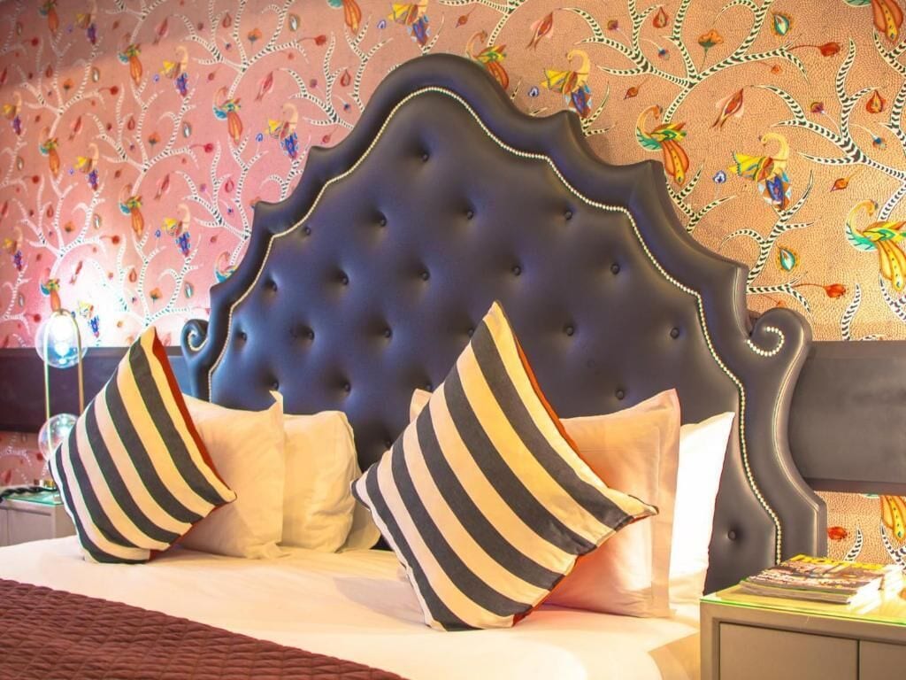 Una cama con cabecera capitonada, almohadas a rayas y un papel tapiz estampado.