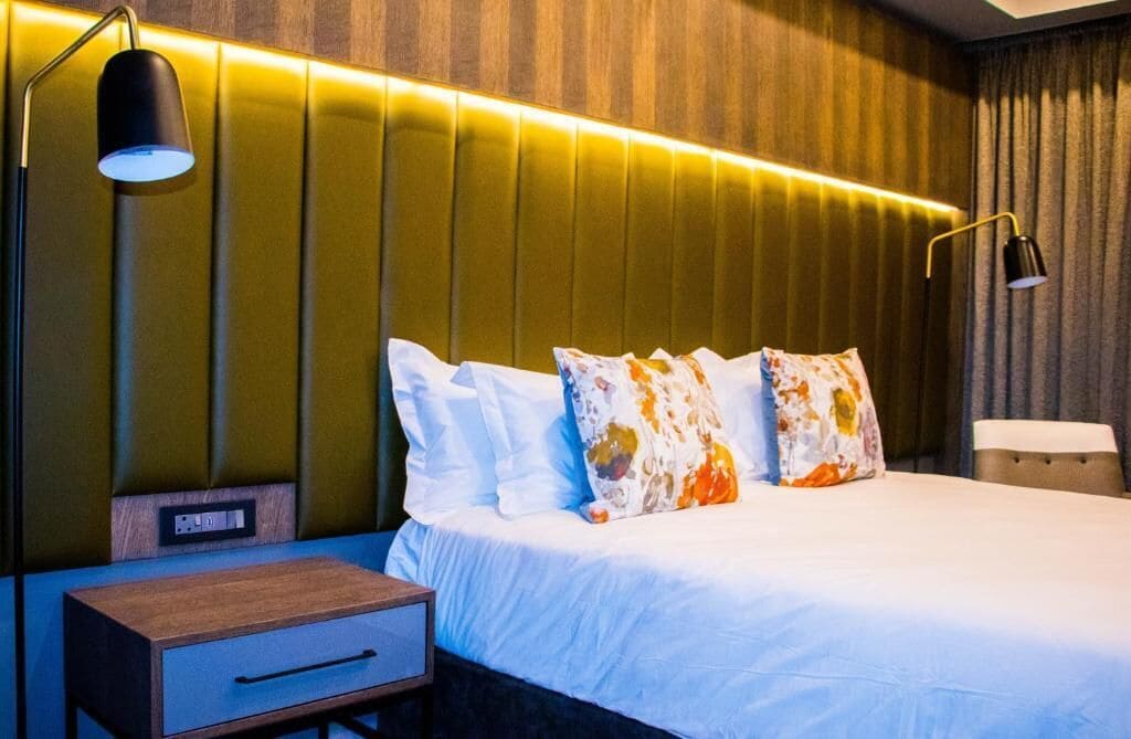 Quarto de hotel com cama, mesas de cabeceira e luminária fixada na parede.