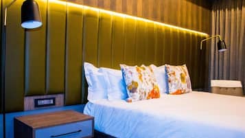 Quarto de hotel com cama, mesas de cabeceira e luminária fixada na parede.