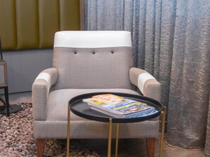 Un sillón gris con un cojín blanco, una mesita negra con revistas y una alfombra estampada.