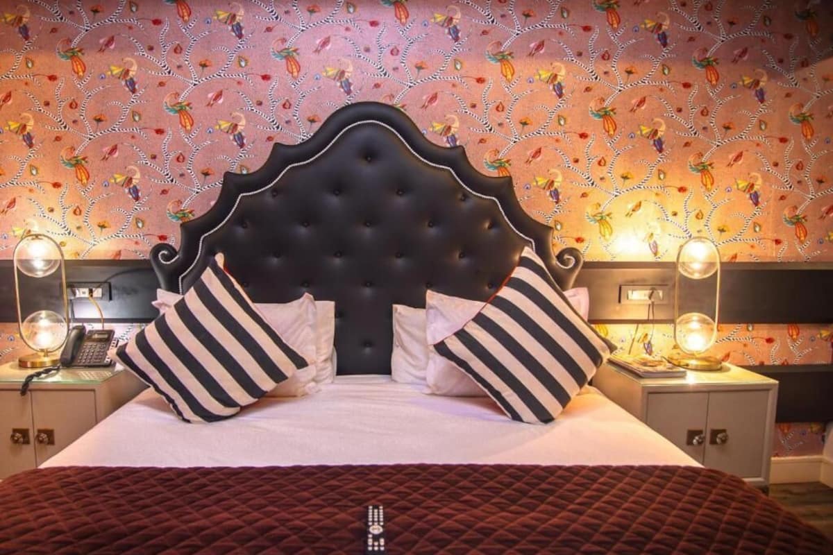 Una habitación de hotel con una cama grande, almohadones a rayas, un cabecero capitonado y papel tapiz estampado.