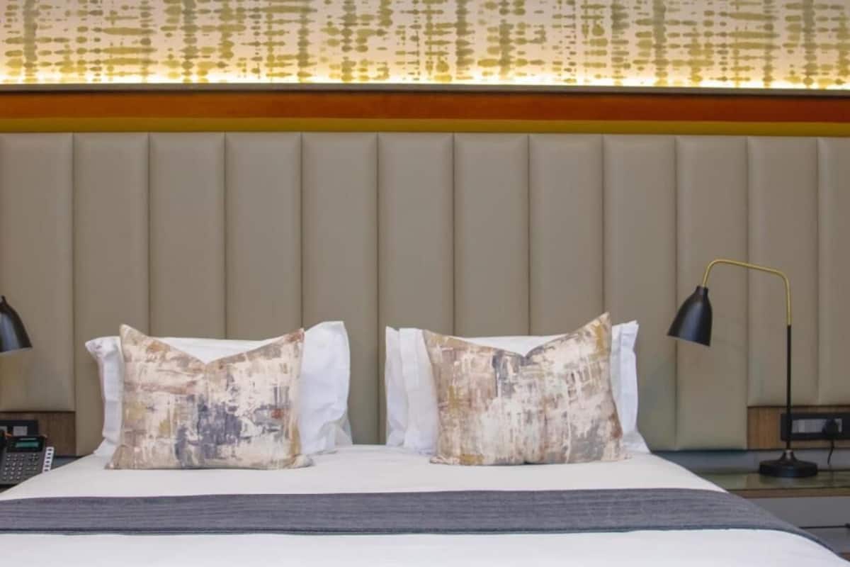Una habitación de hotel con una cama grande, dos almohadas decorativas, una mesita de noche con lámpara y teléfono.