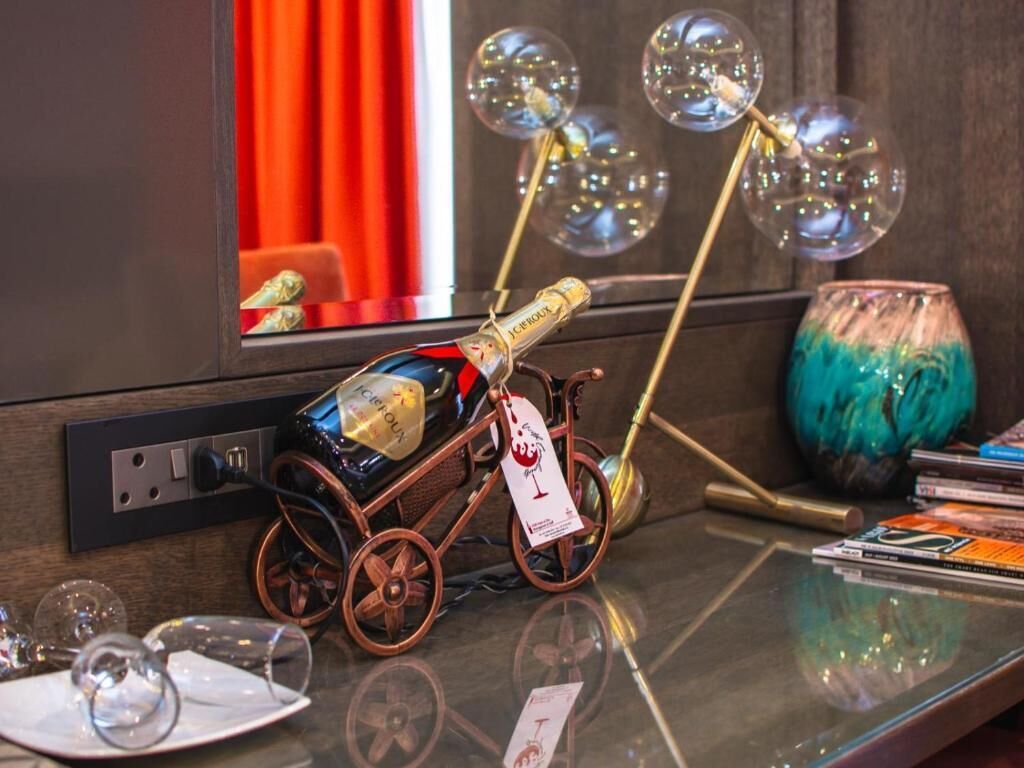 Une table avec une bouteille de champagne, un chargeur en forme de vélo et une lampe décorative ornée d’éléments sphériques.