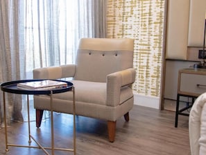 A room with a tufted armchair, a small round table with a magazine, and a patterned wallpaper wall.