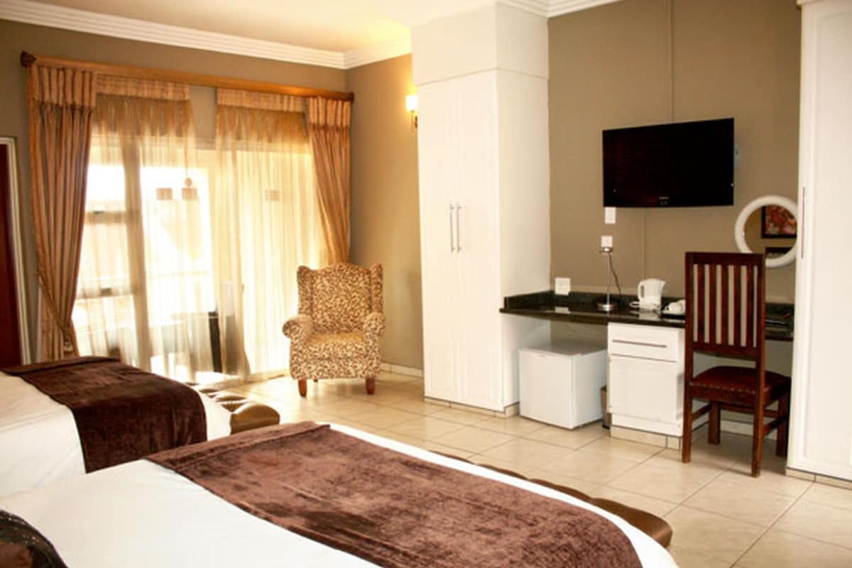 Habitación de hotel con dos camas, un escritorio, una silla, un televisor y una ventana con cortinas.