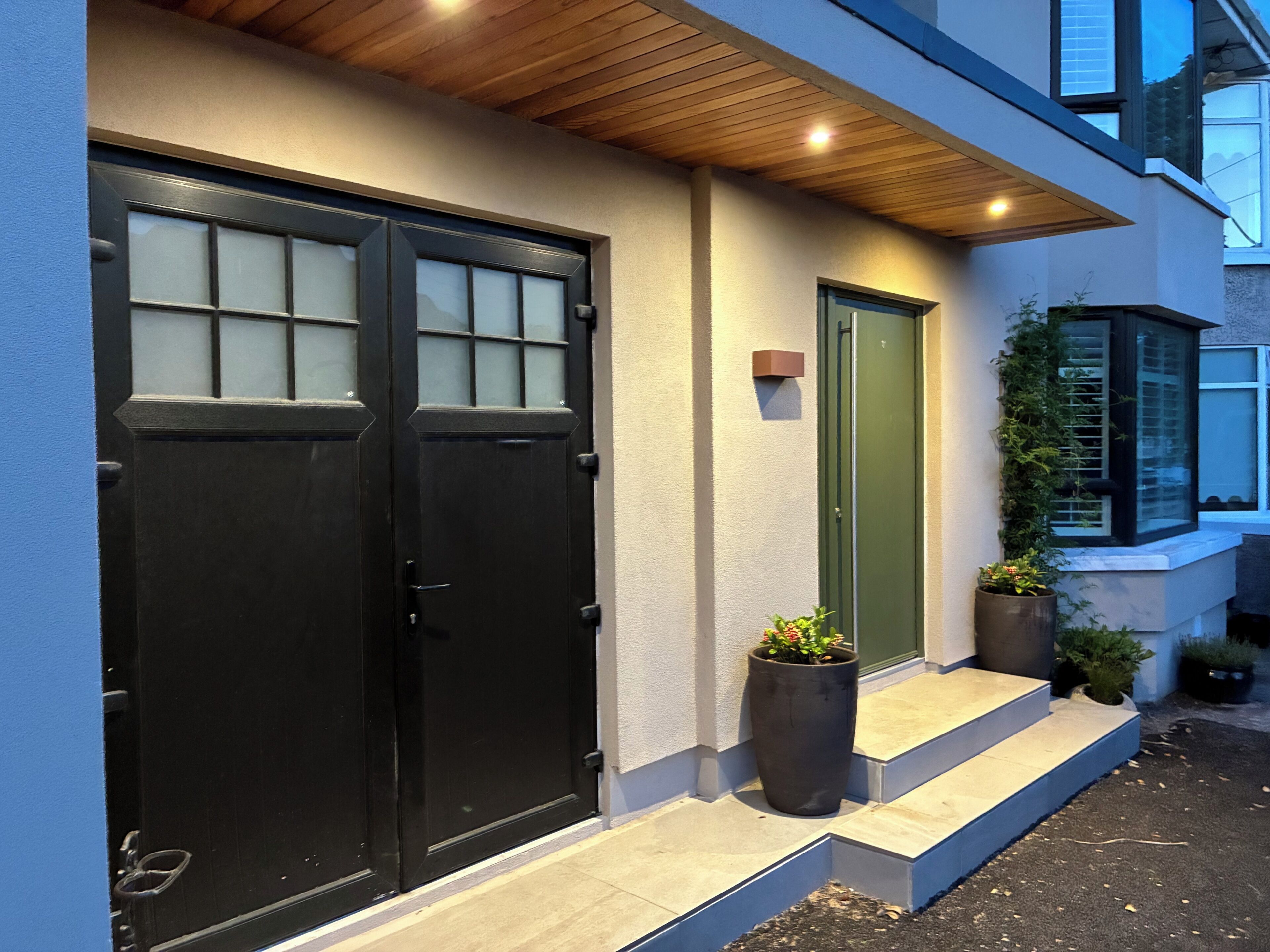 A modern building with two black doors, a green door, and a small set of steps leading to the entrance.