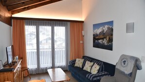 Ein Wohnzimmer mit Sofa, Sessel, Holztisch und Fernseher.