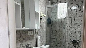 Un baño con lavamanos blanco, espejo y retrete, ducha con puerta de cristal y azulejos estampados.