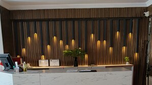 Una recepción con encimera de mármol, listones de madera verticales al fondo y una planta en el mostrador.