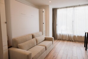 A room with a sofa, a wardrobe, a window with curtains, and a wooden floor. - Stunning, fully equipped studio apartment 250 meters from the beach (Ajaccio)