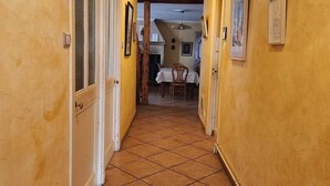 Un corridoio con pavimento piastrellato, travi in legno al soffitto e porte che conducono a una sala da pranzo.