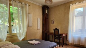 Una camera da letto con un letto, una scrivania, una sedia, una sveglia e una finestra con tende.