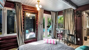 A room with a bed, a desk, and a chair. There is a window with curtains, a door, and a view of the outside.