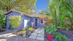 A house with a blue exterior, a paved pathway, and various plants.