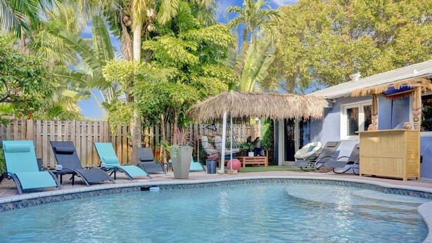 A swimming pool with lounge chairs, a wooden fence, and tropical vegetation.