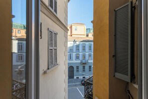 Ein schmaler Straßenblick durch ein Fenster, mit einem geparkten Auto und Häusern mit Rollläden.