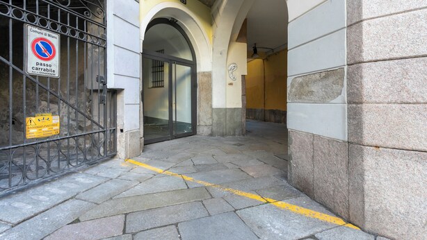 Un callejón estrecho con una reja metálica, un cartel de no estacionamiento y una señal de precaución amarilla.
