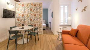 Un espacio habitable compacto con comedor, un sofá, un televisor montado en la pared y una pieza artística de un pájaro en la pared.