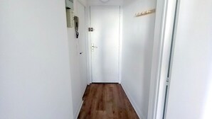 Een smalle gang met houten vloer, witte muren en een deur aan het einde.