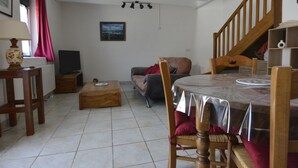 A living room with a wooden dining table, a sofa, a coffee table, a lamp, a TV, and a staircase.