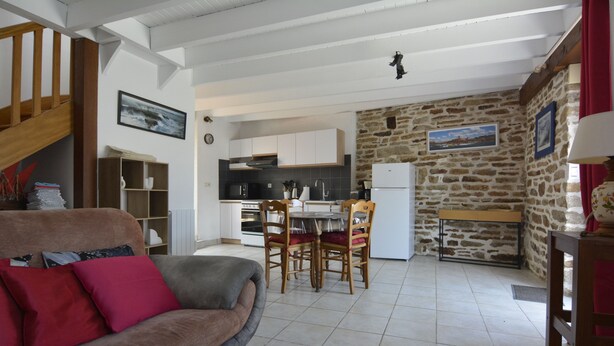 A living room with a sofa, a dining table with chairs, a kitchen area, and a stone wall.