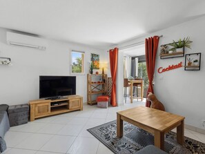 A modern living room with a flat-screen TV, wooden furniture, a dining area, and a balcony with red curtains. - Hameau de Croisette Plage by Interhome (Sainte Maxime)