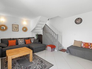 Uma sala de estar moderna com um sofá cinzento, uma mesa de centro de madeira e uma escada que dá para um andar superior.