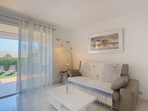 A modern living room with a sofa, a coffee table, a floor lamp, and a window with sheer curtains. - Les Coteaux de la Nartelle by Interhome (Sainte Maxime)