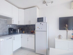 Eine moderne Küche mit weißen Schränken, einer eingebauten Mikrowelle, einem Kühlschrank und einer Kaffeemaschine.