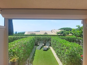 On aperçoit, à travers une porte vitrée, un jardin avec une pelouse, deux chaises longues et, au fond, un bâtiment dont le toit est recouvert de tuiles.