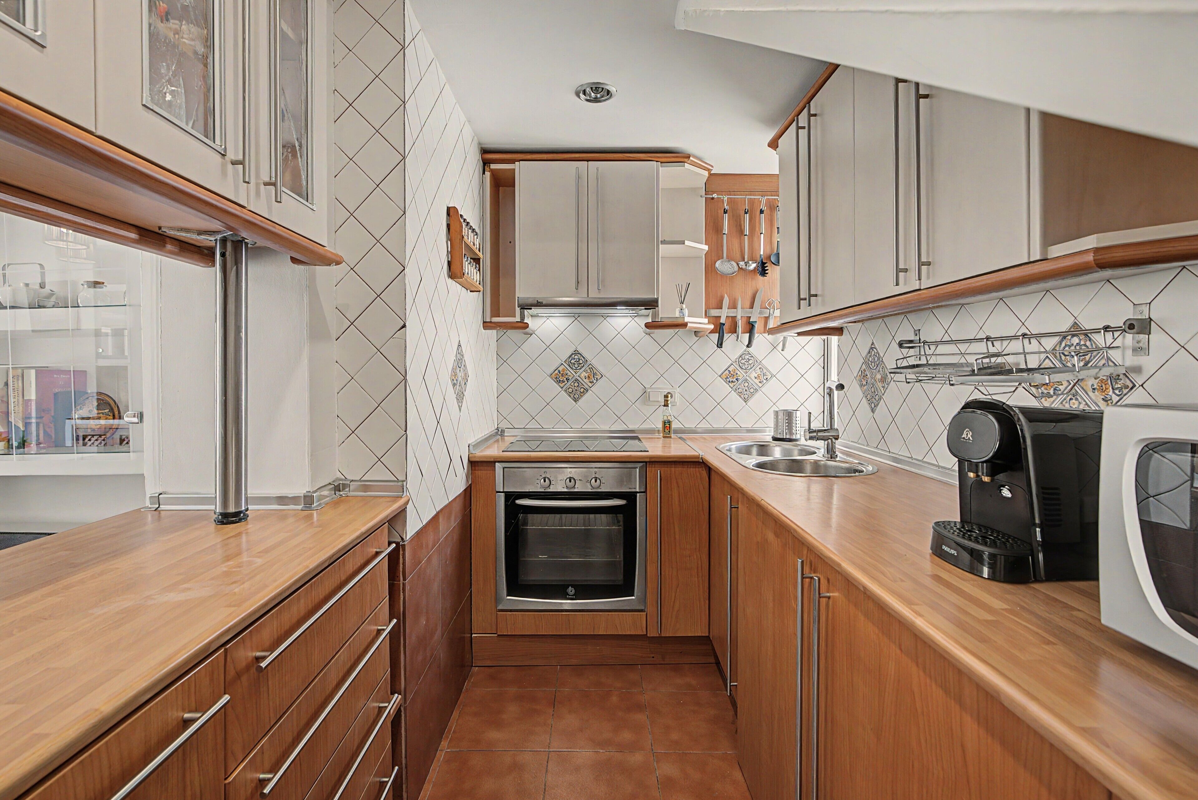 A compact kitchen with wooden cabinets, a built-in oven, a coffee maker, and a tiled backsplash.