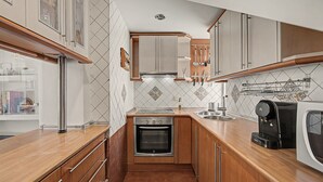 A compact kitchen with wooden cabinets, a built-in oven, a coffee maker, and a tiled backsplash.
