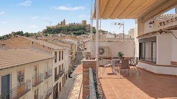 Una terraza con vistas a un castillo histórico en una colina, tejado de baldosas y una mesa con sillas.