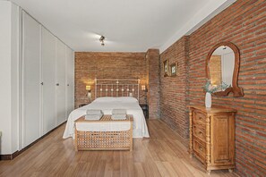 Ein Schlafzimmer mit Backsteinwand, einem hölzernen Bettgestell, einer Holzkommode und einem weißen Kleiderschrank.