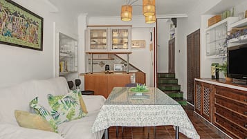 Ein Wohnzimmer mit einer Couch, einem Esstisch und einer Küchenzeile mit Schränken und einer Treppe.