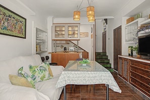 A living room with a sofa, a dining table, and a kitchen area with cabinets and a staircase.