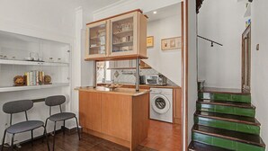 A compact kitchen with a washing machine, a small dining area with chairs, and a staircase with green steps.