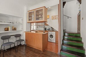 A compact kitchen with a washing machine, a small dining area with chairs, and a staircase with green steps.