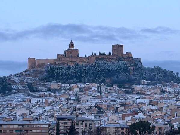 Un castillo histórico en una colina con vistas a un pueblo con tejados cubiertos de nieve.
