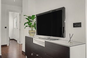 Un salon moderne avec un téléviseur à écran plat fixé au mur, un meuble en bois foncé en dessous et une plante en pot sur la gauche.