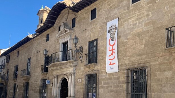 A historic building with a prominent entrance, a balcony, and a banner.