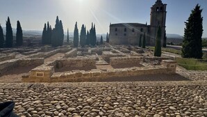 An ancient ruin with stone pathways, a bell tower, and cypress trees.