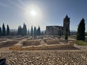 Restes antigues amb camins de pedra, una torre campanar i xiprers.