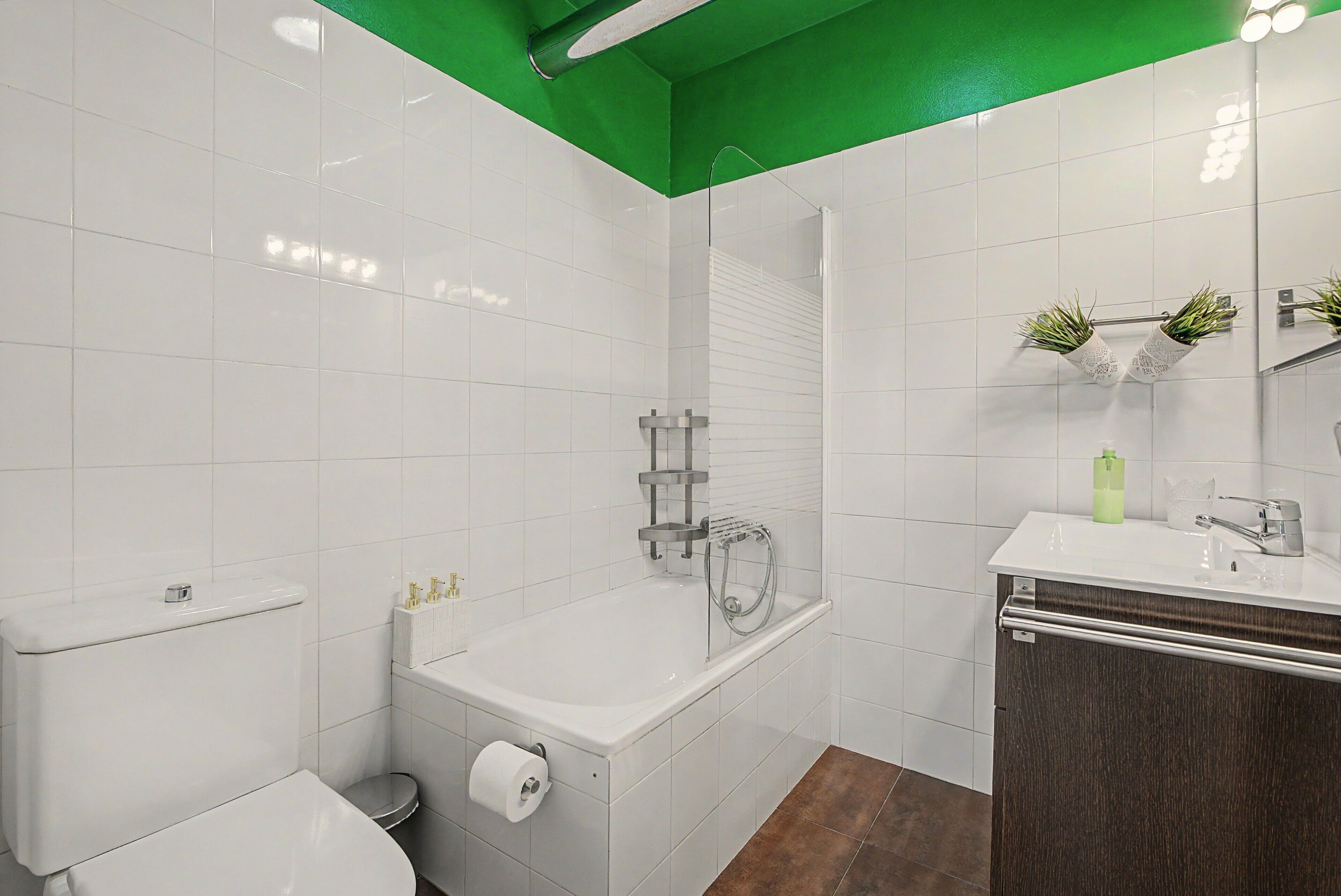 A modern bathroom with white tiles, a bathtub, a toilet, and a sink with a mirror above it.