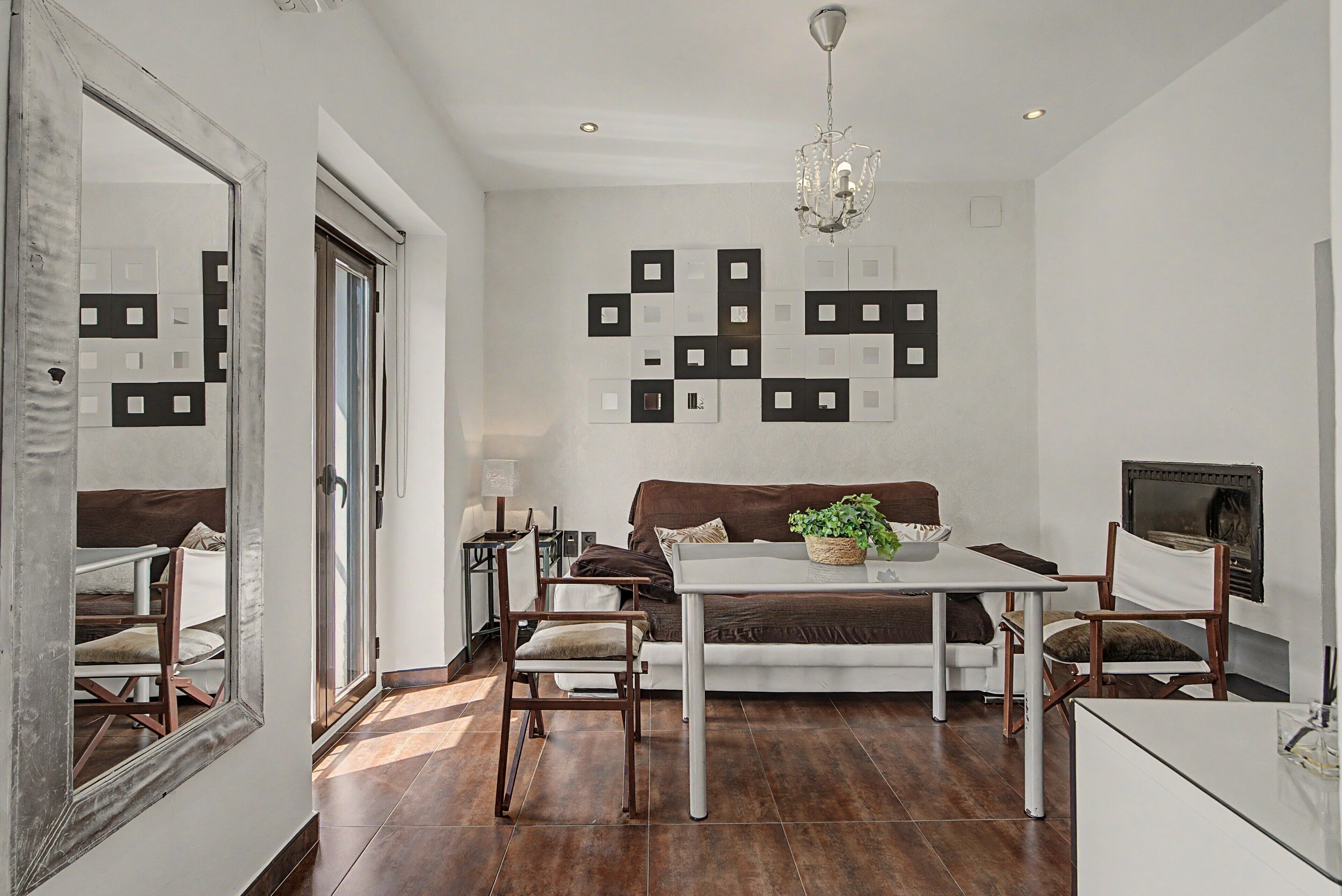 Een moderne woonkamer met een eetgedeelte, een kroonluchter en een grote spiegel.
