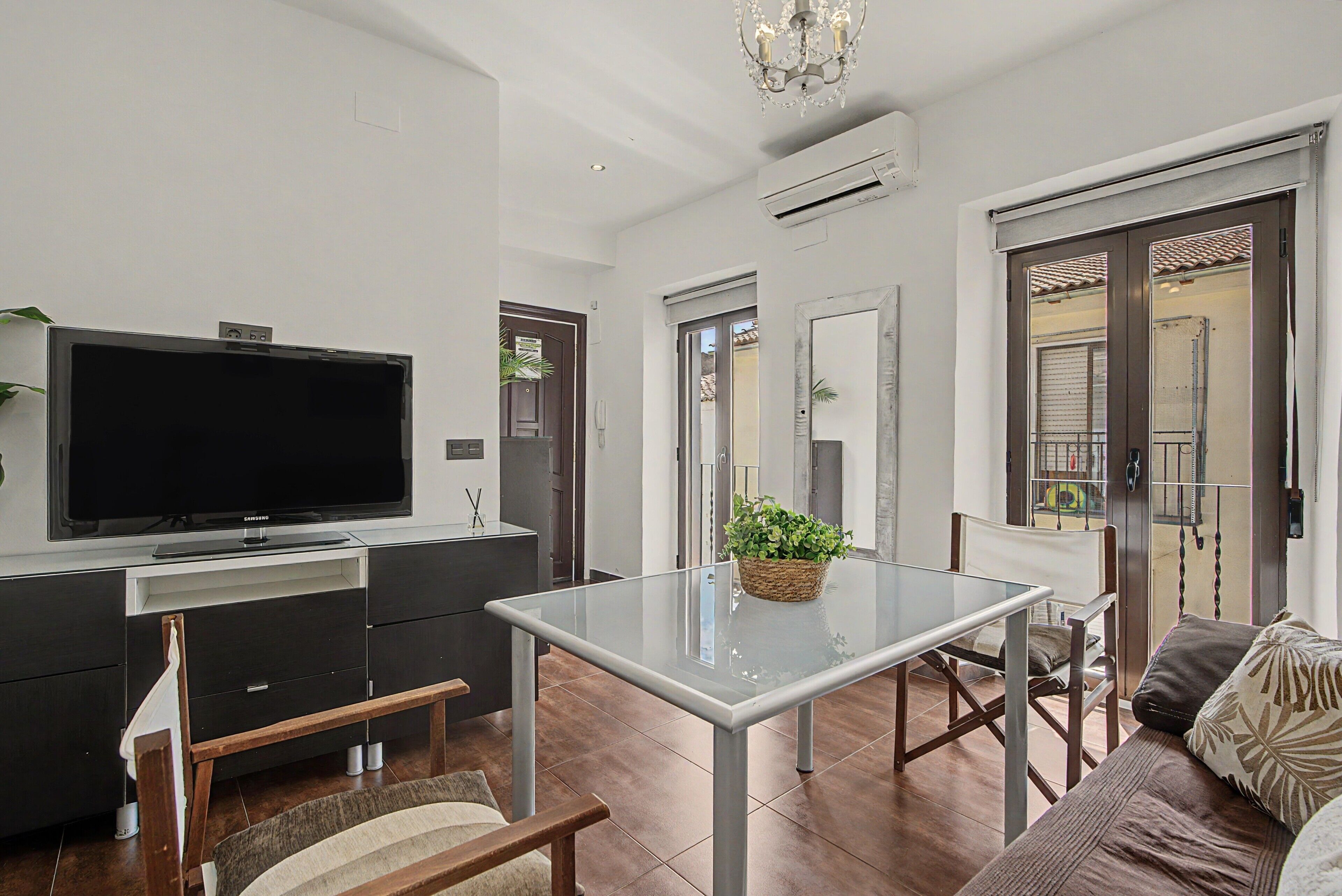 A modern living room with a flat-screen TV, a glass-top dining table, and a sofa.