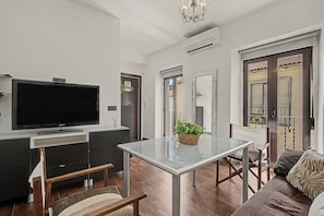 A modern living room with a flat-screen TV, a glass-top dining table, and a sofa.