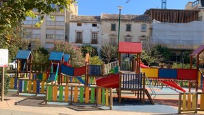 A playground with various play structures, surrounded by buildings and a clear sky.