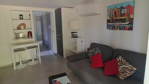 A living room with a grey sofa, a black ottoman, a white table with two stools, a painting on the wall, and a kitchen area in the background. - Near Bordeaux: air conditioning, parking, and a picturesque setting (Latresne)